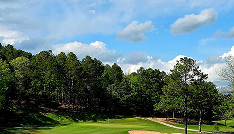 View of golf course fairway with trees, cart path and bunker